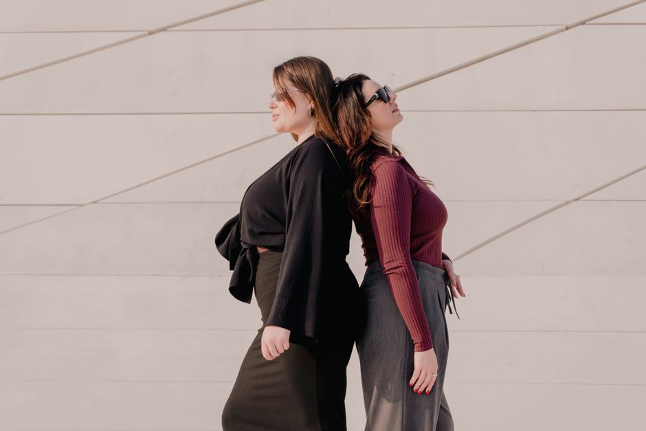 Two fashionable women stand back to back against a modern, minimalist wall. Perfect for lifestyle and fashion themes.