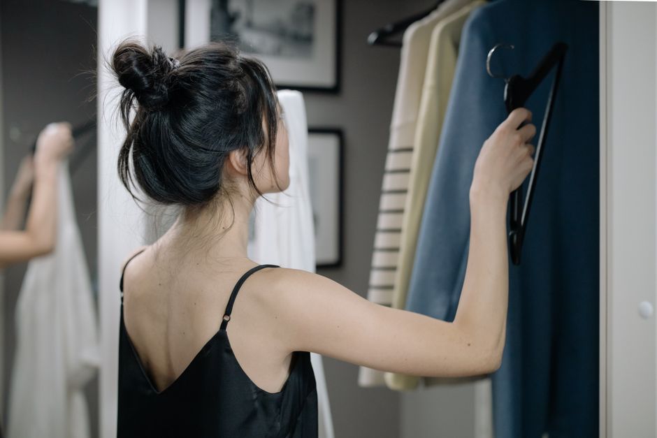 A woman in a nightdress selects clothes from her closet, captured in natural indoor light.