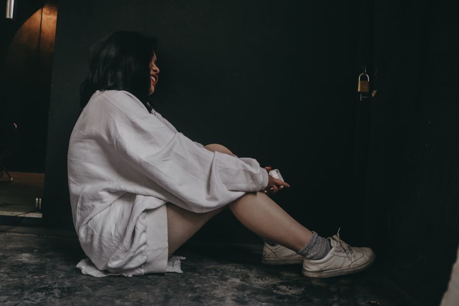 A woman in a white sweater sits indoors, side view, near a padlock, conveying contemplation.