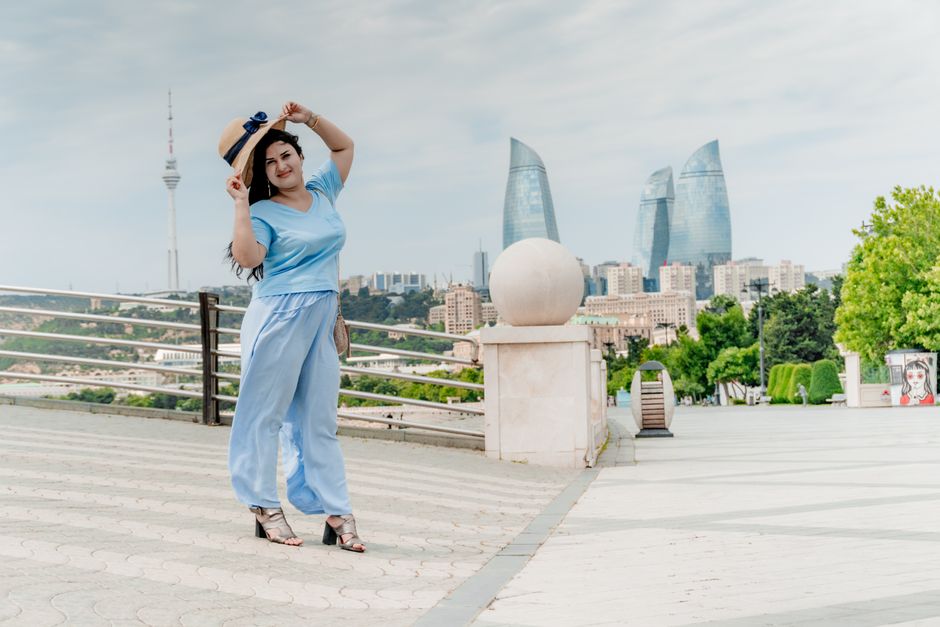 Woman in blue outfit poses against Baku skyline featuring Flame Towers under clear sky.