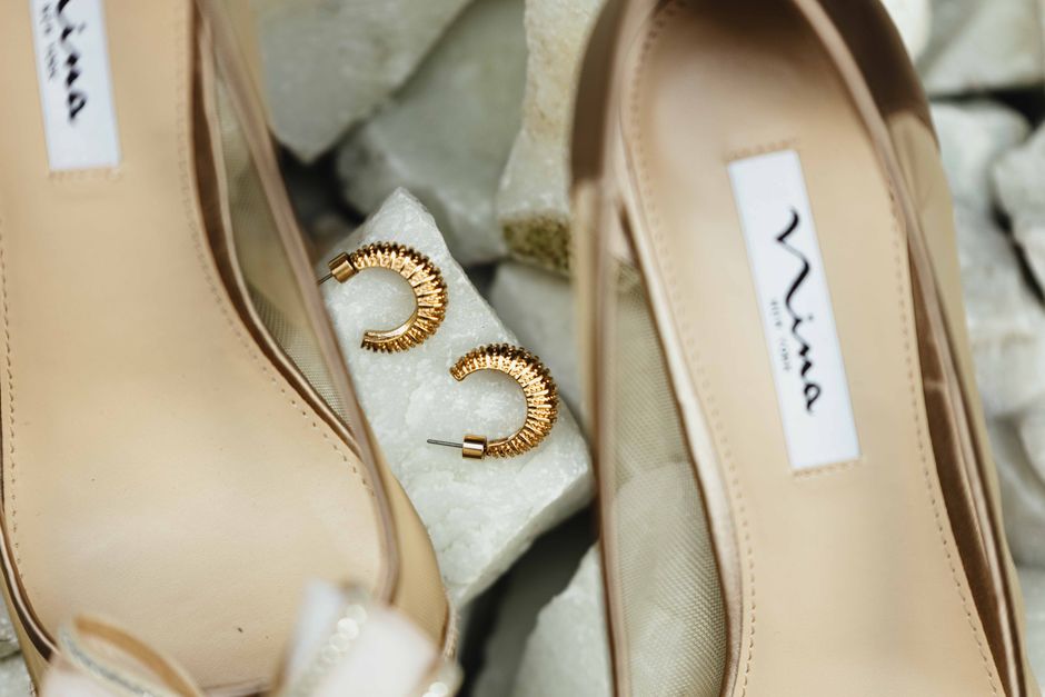 Chic beige heels paired with textured gold hoop earrings on a marble surface, perfect for fashion editorials.