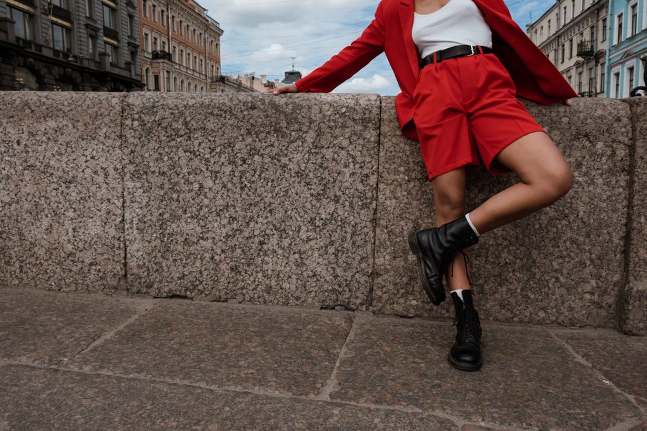 Person in a vibrant red suit leaning on a granite embankment in a cityscape background.