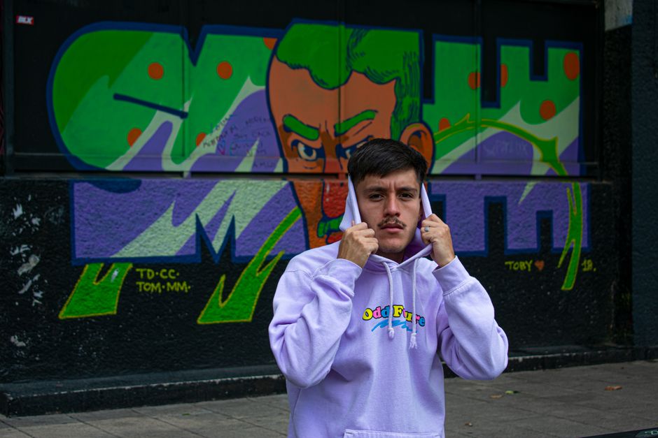 A young man in a hoodie poses confidently in front of vibrant street art in Mexico City, CDMX.