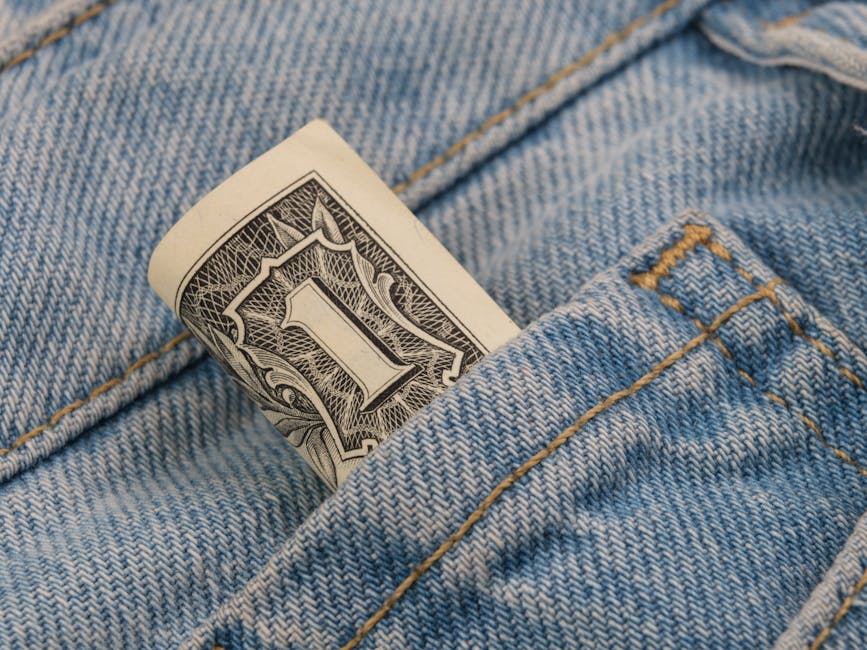 Close-up of a rolled dollar bill tucked into a denim pocket, symbolizing savings and finance.