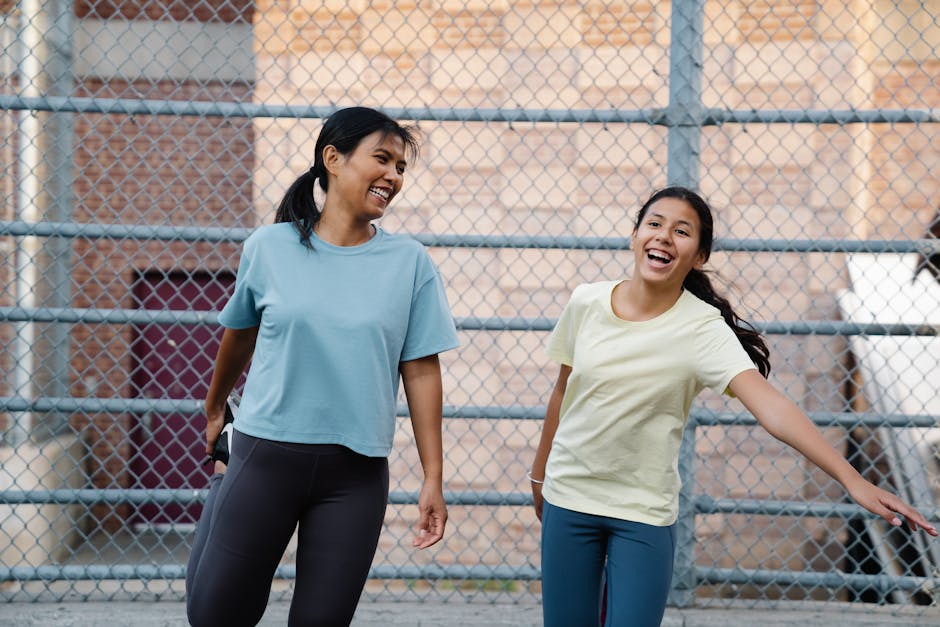 Two women laughing together outdoors, wearing casual T-shirts, joyful moment. Urban setting.
