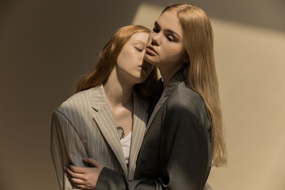 Two women in stylish suits share a tender embrace, showcasing elegance and connection.