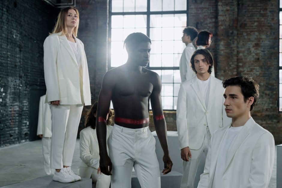 A diverse group of people in white clothing poses in an industrial space, highlighting cultural diversity.
