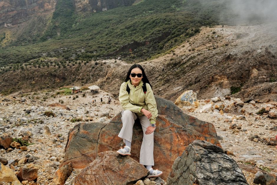 A woman sitting on a rock in a rugged mountain landscape, looking relaxed and adventurous.