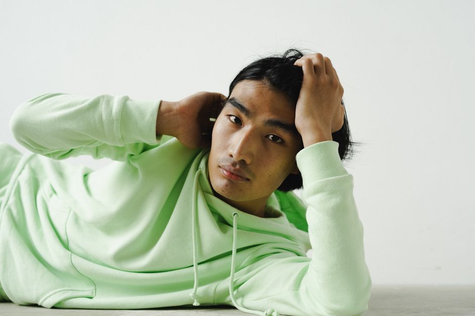 Asian man in a green hoodie lying down indoors, studio setting.