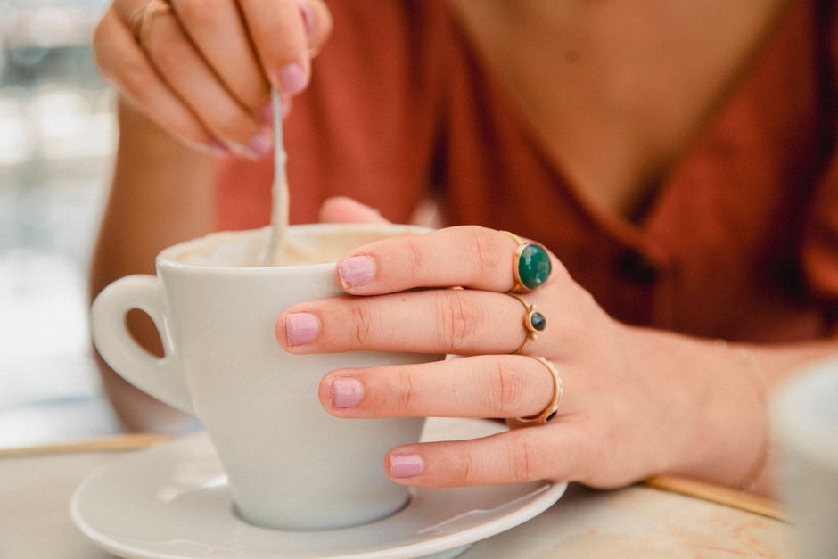 A person stirring a cappuccino in a white cup with elegant rings on fingers, capturing a cozy coffee moment.