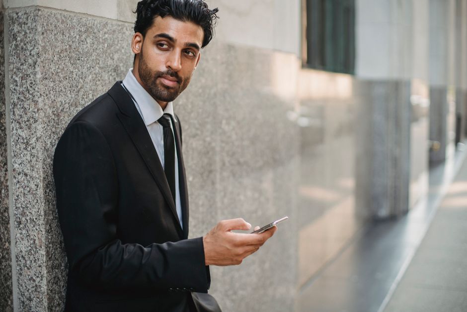 Professional man in suit texting outside in a city environment, leaning against a wall.