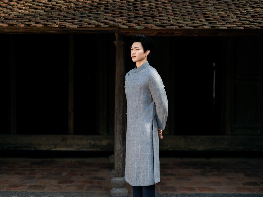 Portrait of an adult in traditional Asian attire standing outdoors with serene expression.