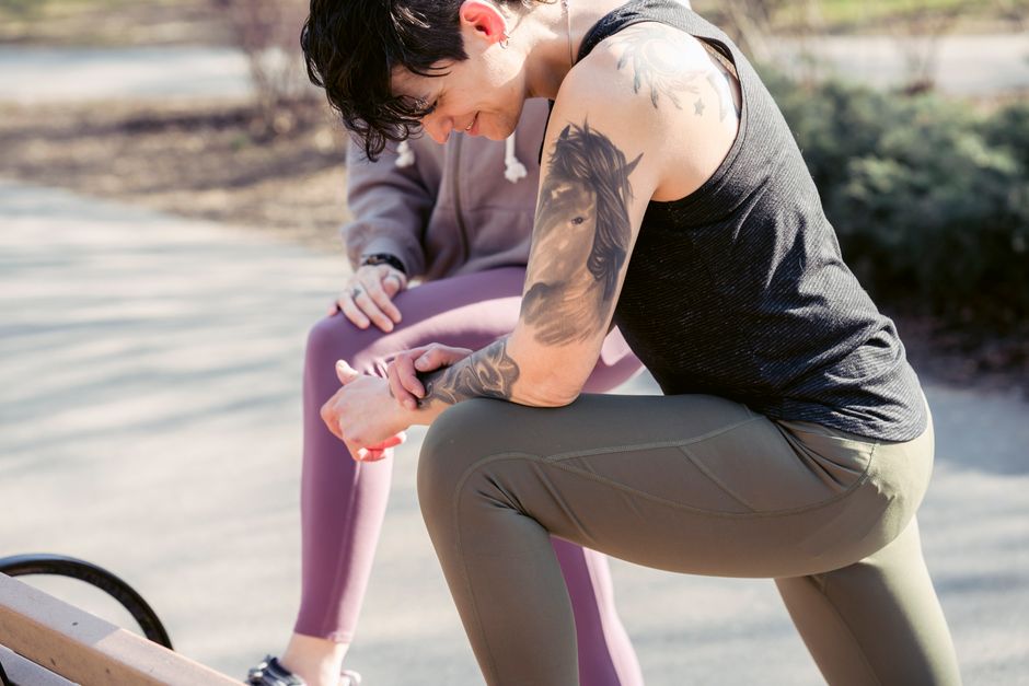 Ladies in sportswear doing exercises on bench in park near road and plants in city street in sunny day