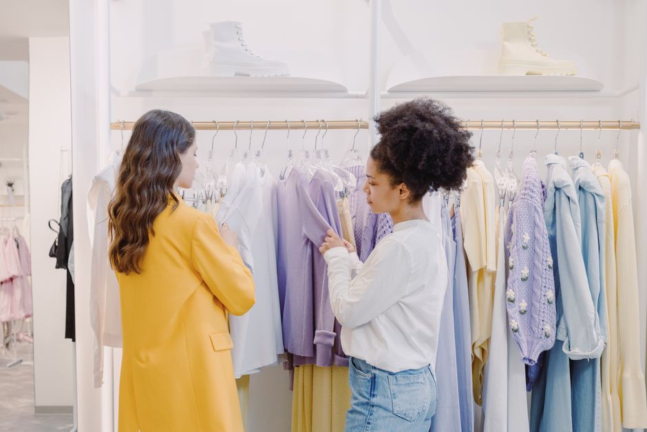 Two women selecting clothes in a chic boutique, discussing fashion choices.