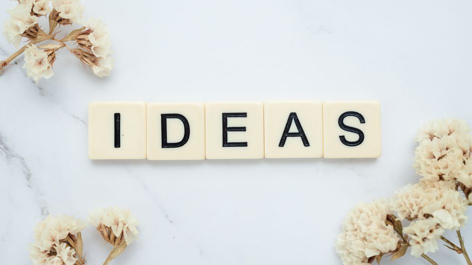 Scrabble tiles spelling 'IDEAS' on a marble surface surrounded by white flowers, inspiring creativity.