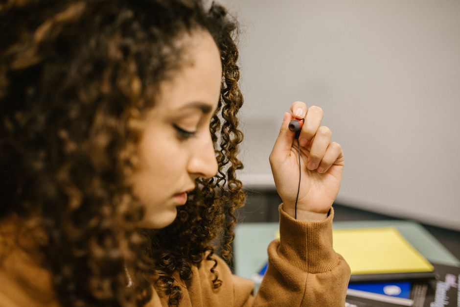A woman attentively holding an earphone, suggesting focus in a classroom or study environment.
