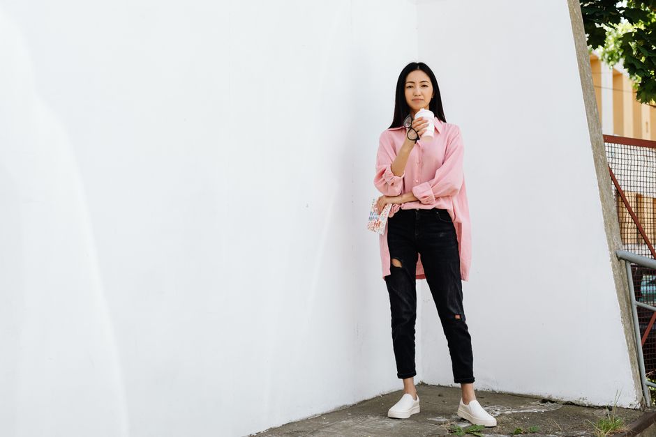 Stylish Asian woman in casual wear posing outdoors while enjoying a coffee.