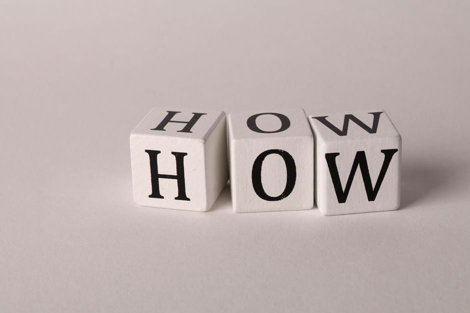 Close-up of white wooden cubes with the letters 'H', 'O', and 'W' arranged on a neutral background.