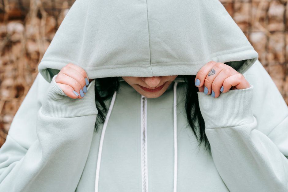 Crop unhappy female covering lowered head with hood in autumn forest in daylight
