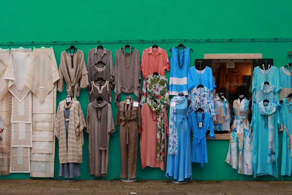 Vibrant clothing display against a green wall in Venice, Italy, showcasing diverse fashion styles.