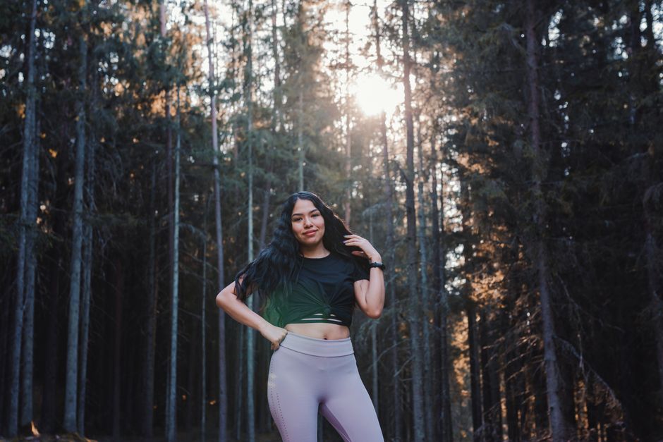A woman in activewear poses confidently in a sunlit forest, showcasing modern sport fashion.