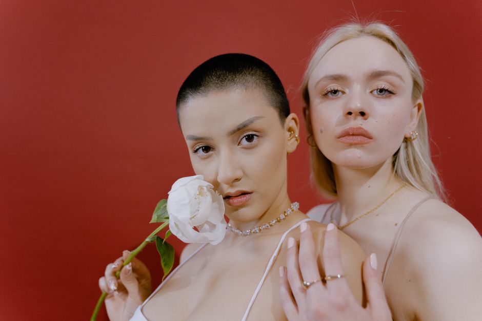 Studio portrait of two women against a red background, emphasizing elegance and femininity.