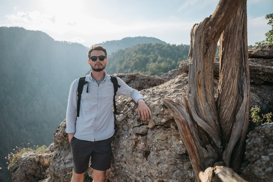 Man poses on a rocky mountain path with stunning countryside views, embracing adventure in nature.