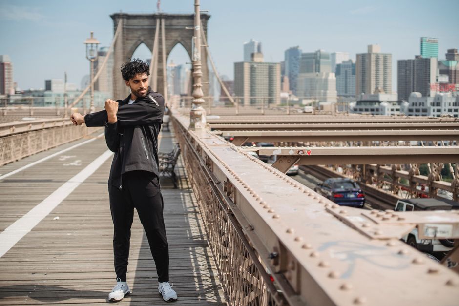 Man stretching on Brooklyn Bridge in sportswear, urban fitness in New York City.