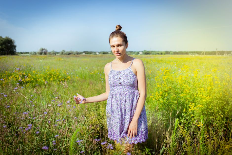 A young woman in a floral dress stands in a sunny meadow in Kherson, Ukraine, surrounded by wildflowers.