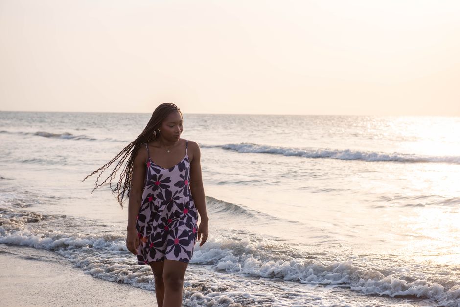 A serene beach scene with a young woman walking along the shore at sunset.