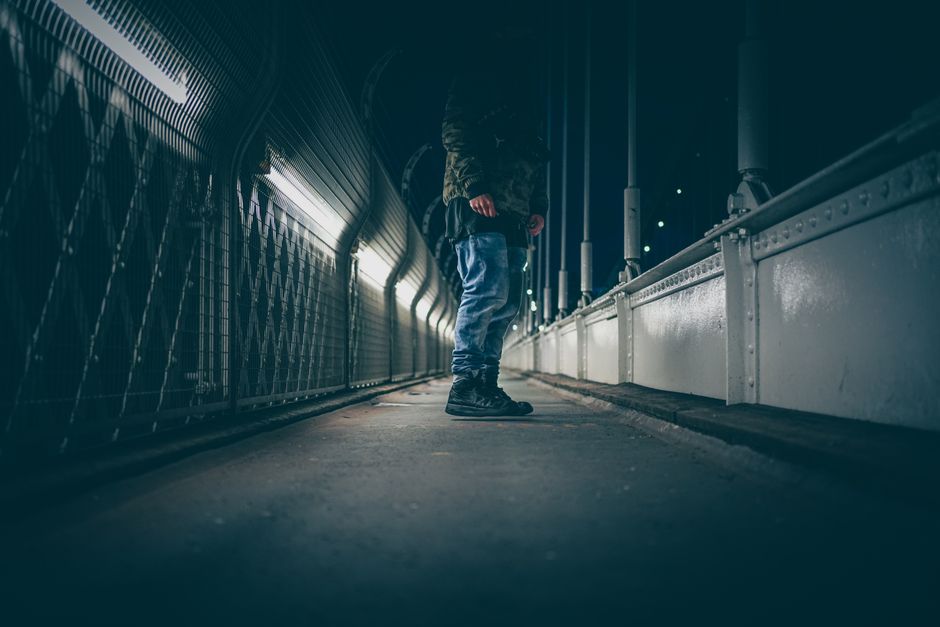 A person casually walks on a bridge at night in Leigh Woods, UK, surrounded by urban lights.