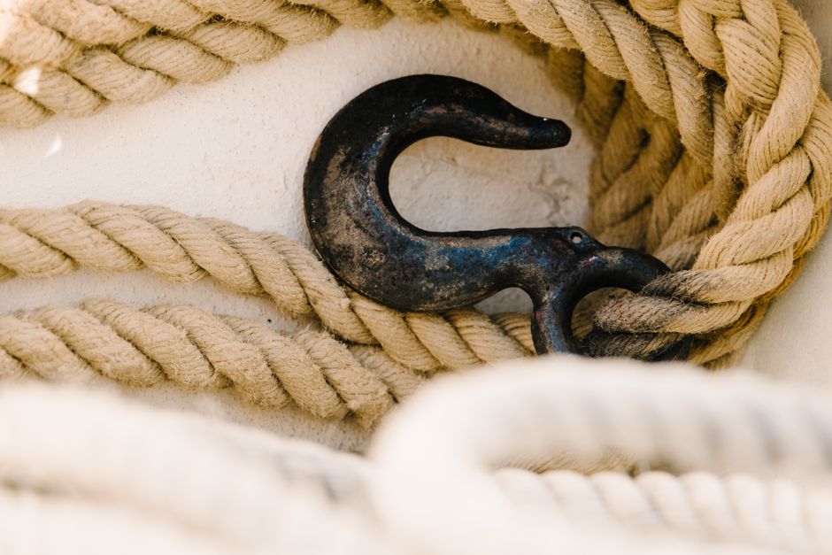 Close-up of a rustic metal hook entwined with thick ropes on a white surface, emphasizing texture.