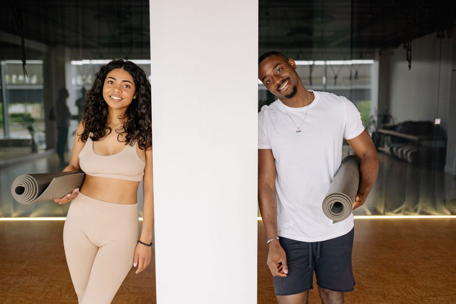 Cheerful couple with yoga mats posing in a modern studio environment.