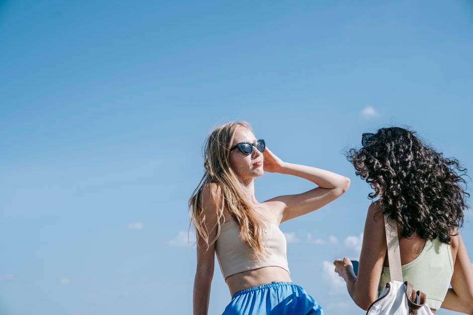 Two women enjoying a sunny day outdoors with clear blue skies, wearing casual summer outfits.