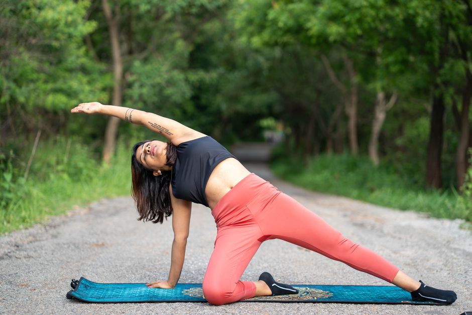 A woman performing a yoga stretch on a mat in a lush outdoor setting, conveying a sense of relaxation.