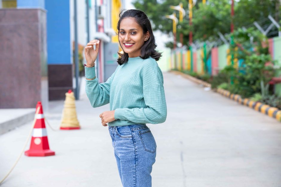 A young woman in a casual teal sweater poses confidently outdoors, exuding happiness.