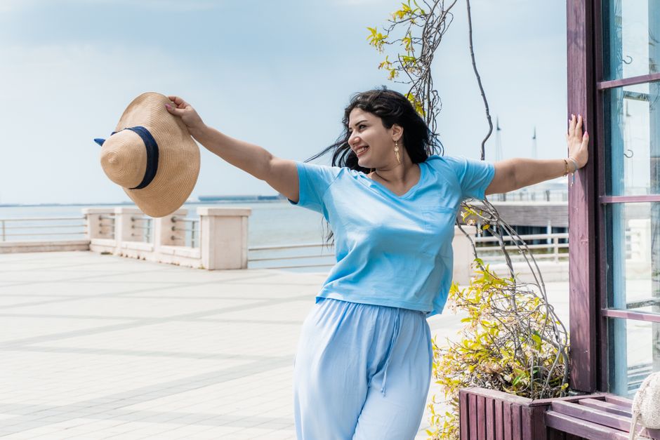 Smiling woman in Baku, embracing summer with a hat, enjoying the seaside view and warm weather.