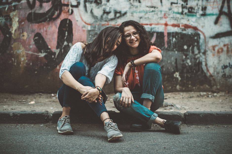 Two women laughing and enjoying each other's company on a graffitied street.