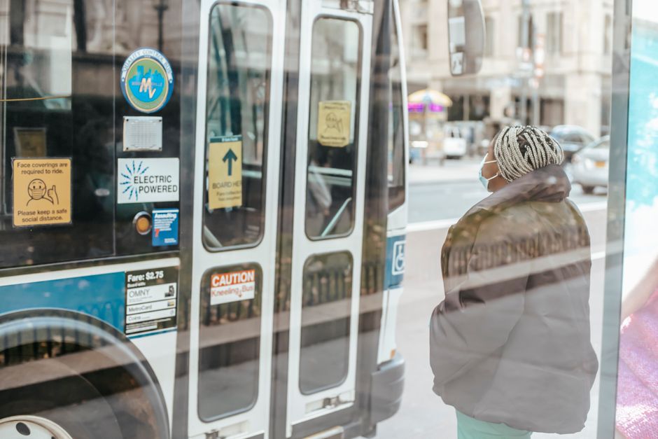 Through glass wall back view of anonymous ethnic female medic standing against public transport in town