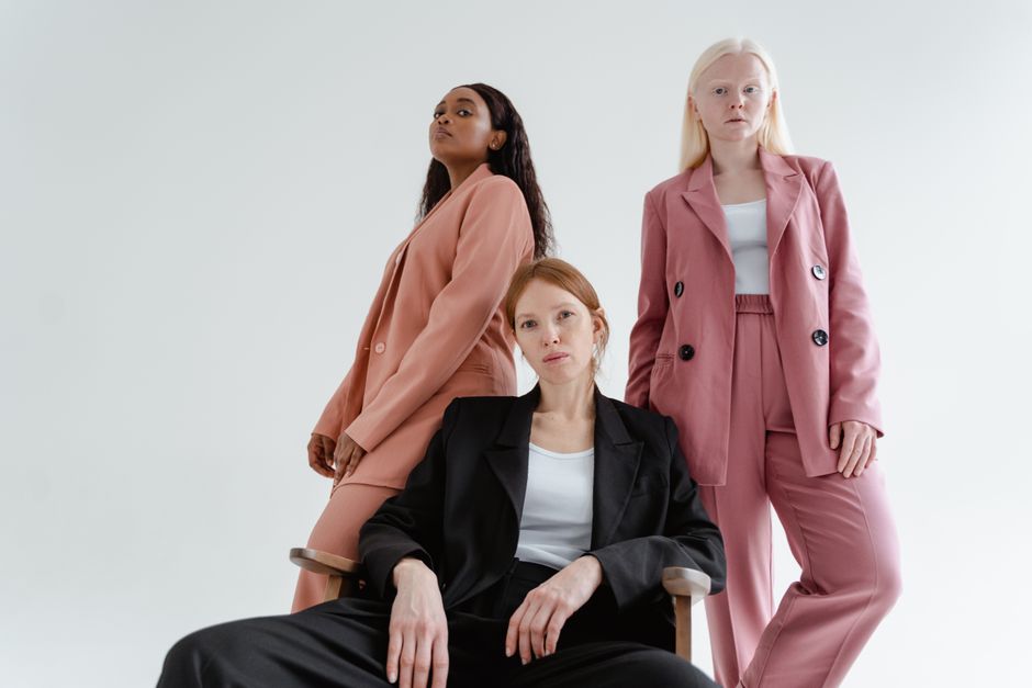 Three diverse women posing confidently in stylish blazers in a white studio setting.