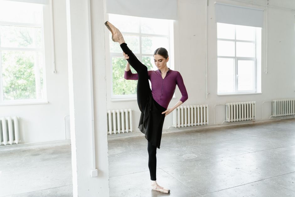 Graceful ballerina in vibrant studio performing a high leg stretch pose.