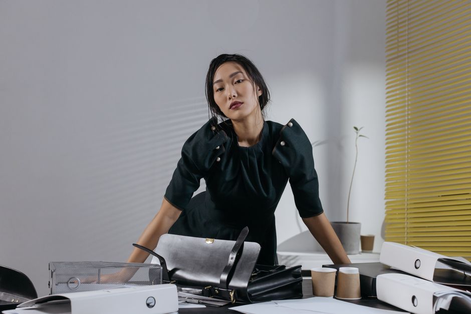 Asian woman in black dress posing confidently in a stylish office setting with modern decor.