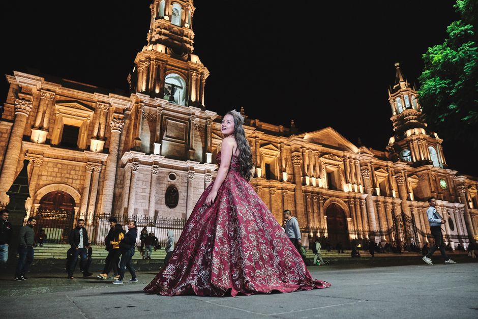Young woman in glamorous red gown posing at night by a majestic cathedral.