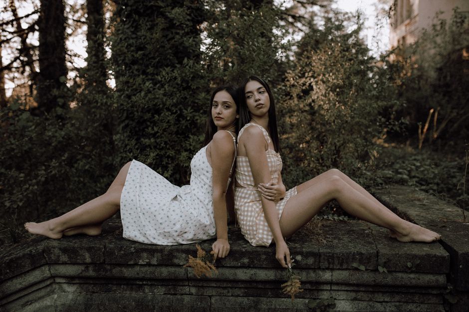 Artistic portrait of two women in elegant dresses sitting in a natural setting, exuding elegance.