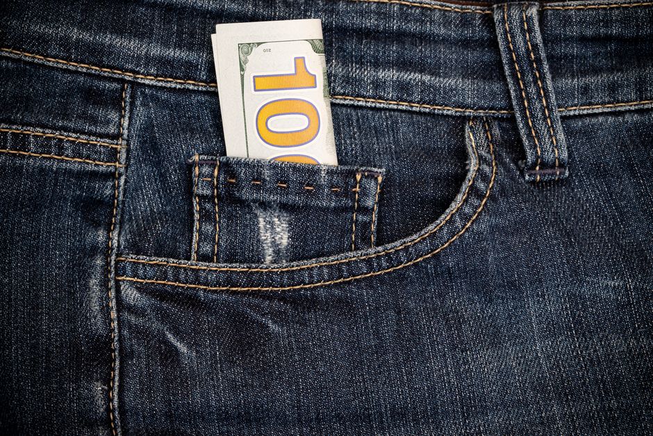 Close-up of blue denim jeans with a $100 bill in the pocket, symbolizing financial savings.