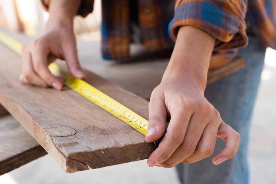 Close-up of hands measuring a wooden plank with a tape measure in a carpentry setting.