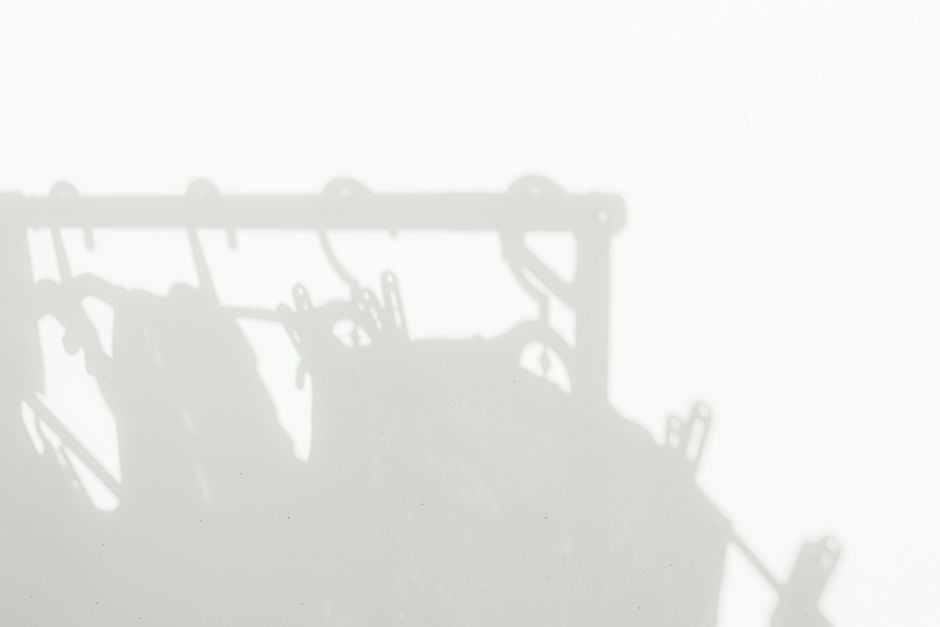 Minimalistic shadow of clothes and hangers on a white wall, creating an abstract artistic backdrop.