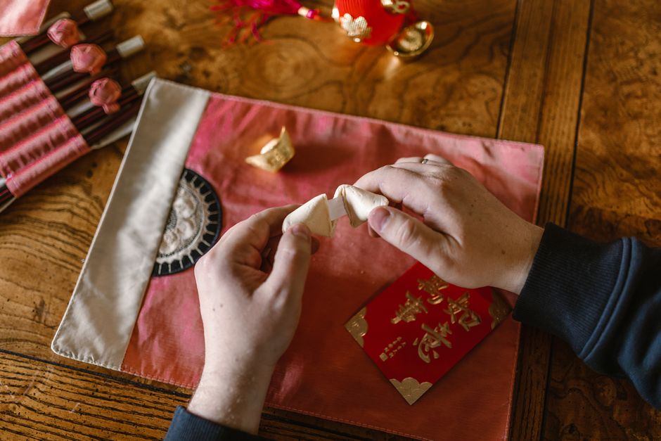 Hands opening a fortune cookie during Chinese New Year celebration on a decorative table.