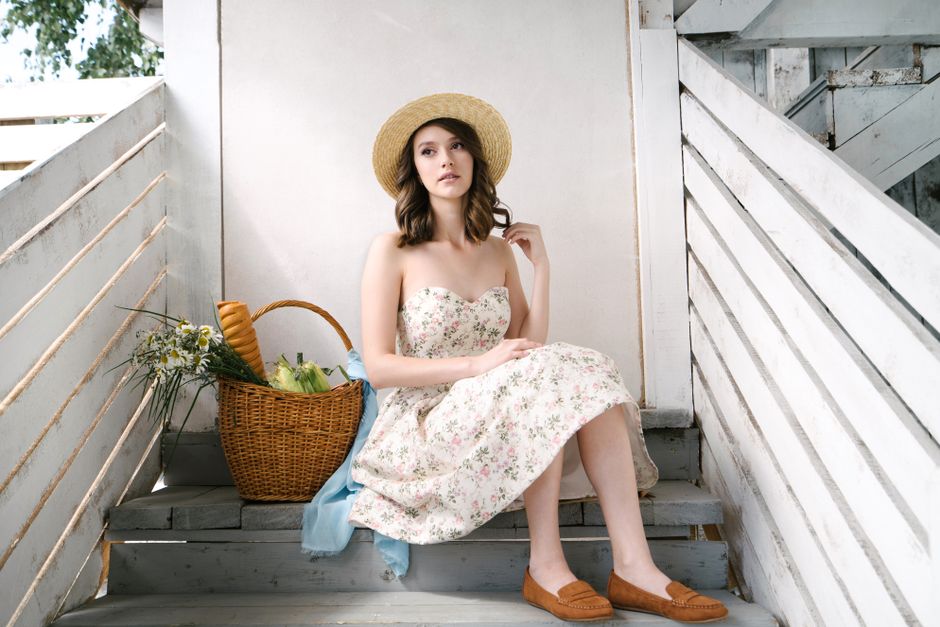 Woman in a floral dress and straw hat seated on stairs with a basket of groceries.
