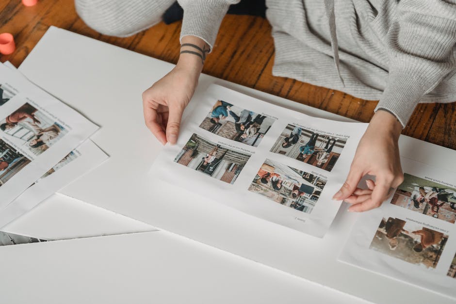Crop faceless person gluing printed images on papers while sitting on floor in light room